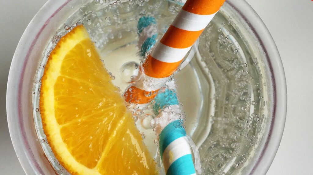 closeup of seltzer glass with orange garnish and two straws