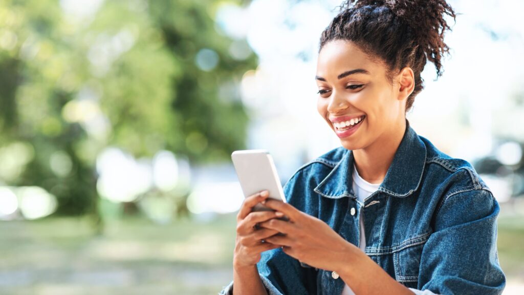 woman smiling while looking at her smartphone outdoors