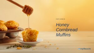 Honey cornbread muffins with honey drizzling from a dipper on a light wood surface